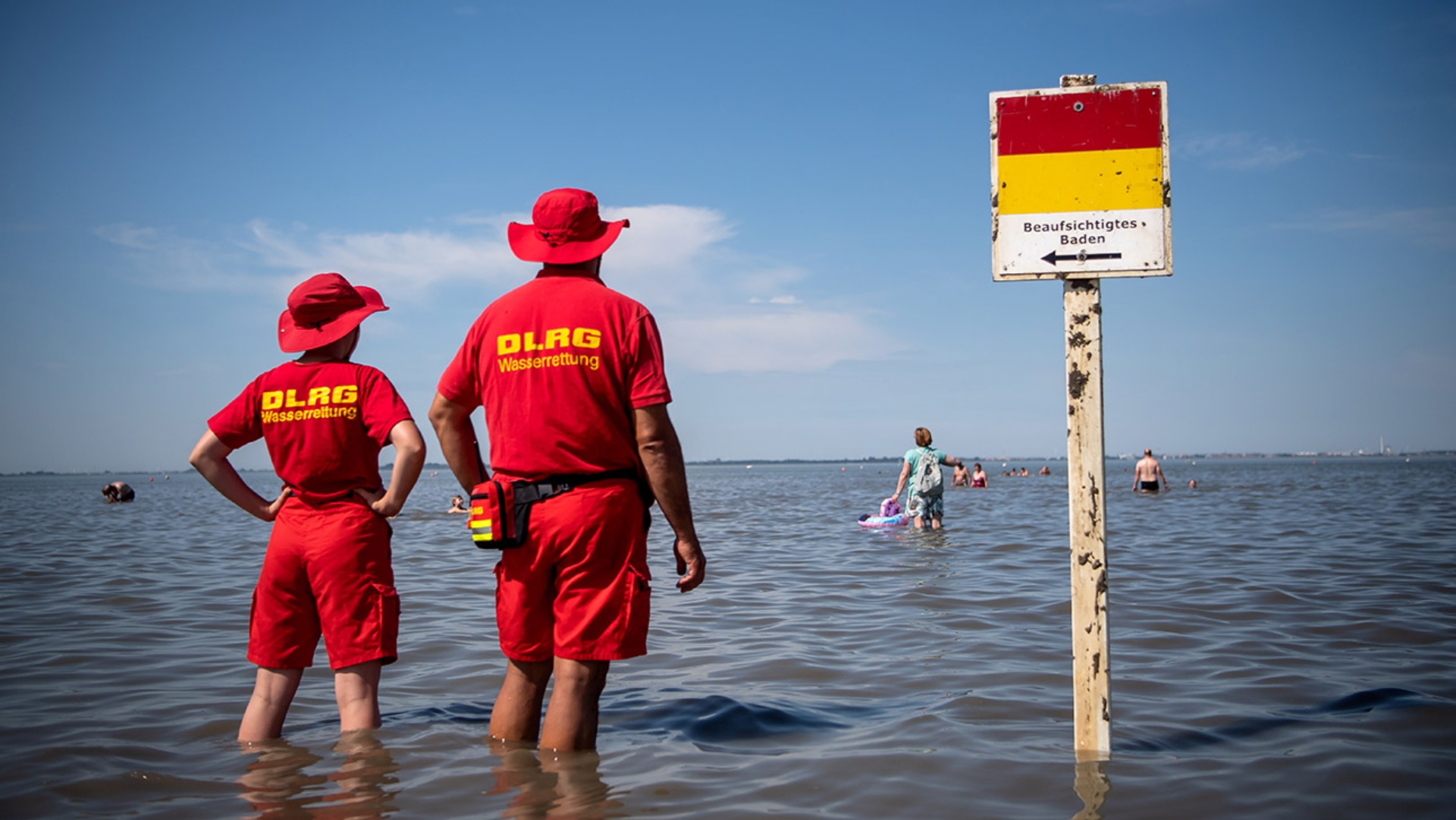 Zwei Mitglieder der DLRG (Deutsche-Lebens-Rettungs-Gesellschaft) stehen im knietiefen Wasser und blicken aufs Meer.