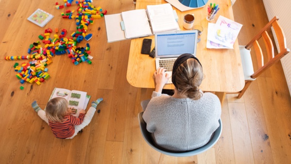 Homeoffice Kinderbetreuung Work-Life-Balance © Foto: dpa, Julian Stratenschulte Ein zweijähriges Kind spielt im Wohnzimmer, während seine Mutter Zuhause im Homeoffice an einem Laptop arbeitet.
